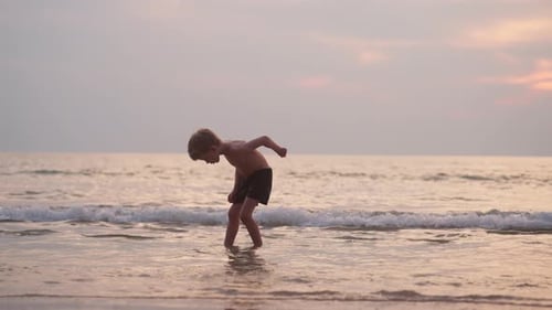 Child Plays in Gentle Waves on Beach at Sunset