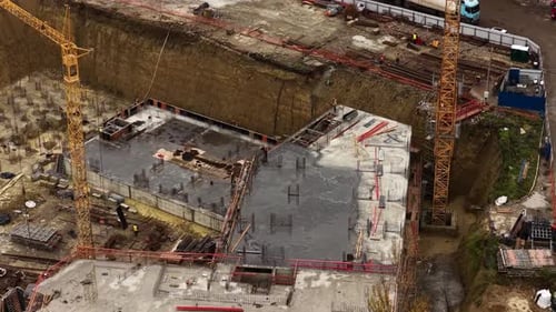 Aerial view of concrete foundation slabs, rebar columns and tower crane structure inside a large dee