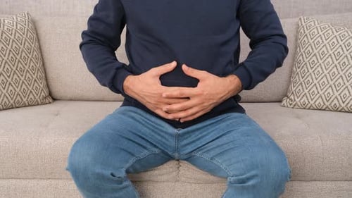 Man Holds Stomach, Experiencing Discomfort on Couch