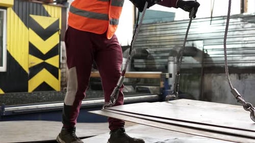 Ein Arbeiter bewegt große industrielle Metallteile mit einem ferngesteuerten Regalkran.