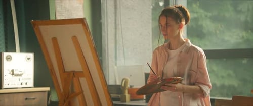 Stylish Young Woman Artist Painting Picture on Canvas Hold Brush and Palette in Art Studio Workspace