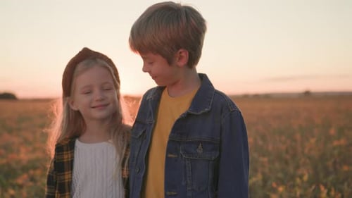 Two Smiling Children in a Grassy Field at Sunset