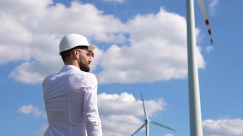 Renewable Energy Engineer Looking at the Sky with a Wind Power Generator in the Background