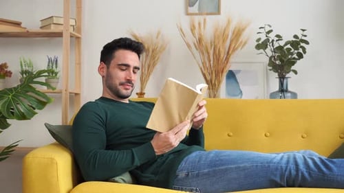 Man Reading a Book on Yellow Couch Indoors
