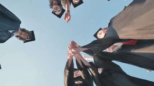 Young Graduates in Caps and Gowns Come Together in a Circle to Celebrate Their Achievement By