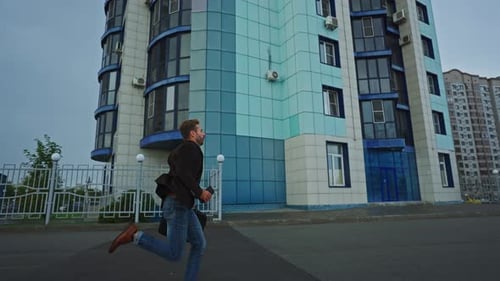 Man Rushes with Coffee By a Modern Apartment in the Morning