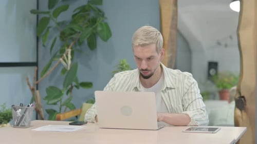Joven moderno escribiendo en la computadora portátil en la oficina