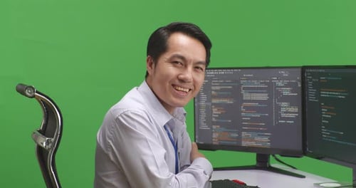 Man Developer Smiling To Camera While Write Code With Multiple Computer Screens In Green Screen