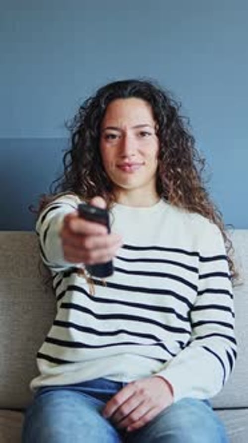 Woman sitting on sofa is changing channels