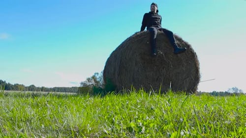 Man Sits on Hay Bale in Rural Field