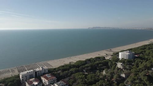 Low aerial retreats over resort hotels from quiet sandy Adriatic beach