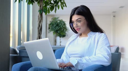 Happy Young Girl Working at a Coffee Shop with a Laptop