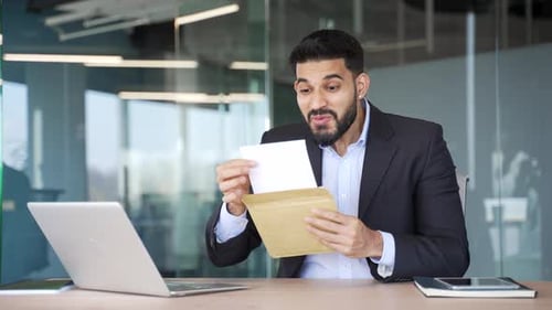 Smiling surprised businessman reading letter with great news sitting at workplace in business office