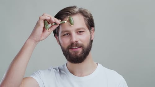Male Skincare Beauty Concept Caucasian Cheerful Attractive Young Man Massaging Face with Green Stone