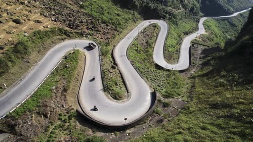 Estrada sinuosa de montanha com veículos navegando em curvas acentuadas, vista aérea