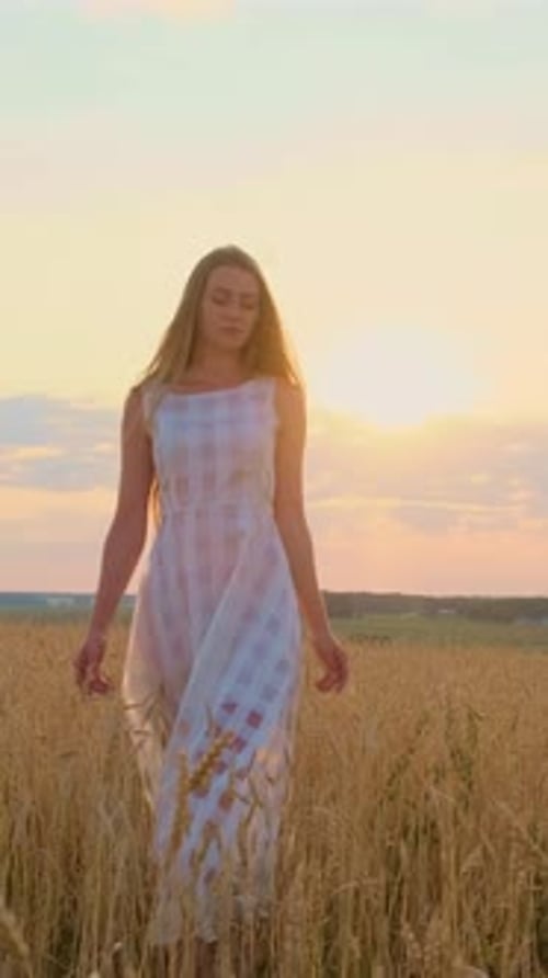 Young Woman in Flowing White Dress Stands in Golden Wheat Field During Sunset Capturing Serene