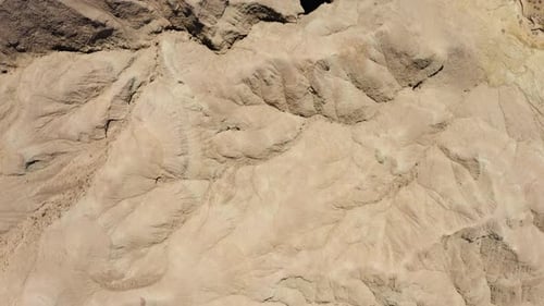 Flying over the sandy textured landscape in a desert environment where there are no plants or trees;