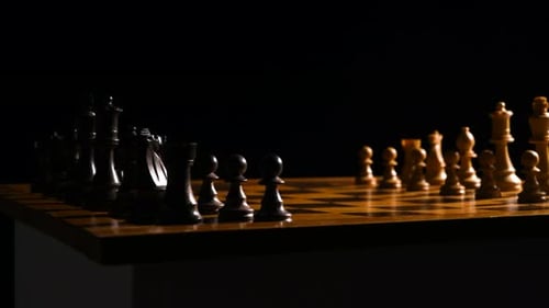Filmaufnahme von Schachfiguren auf einem Schachbrett, der Hintergrund ist schwarz und die Lichtquelle ist com