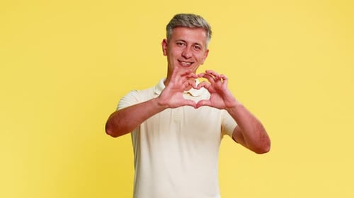Smiling Man Makes Heart Shape with Hands on Yellow