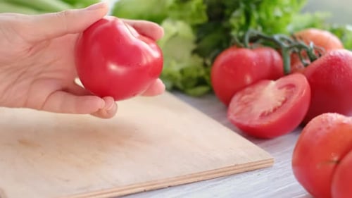 Tomato Held in Hand over Wooden Cutting Board
