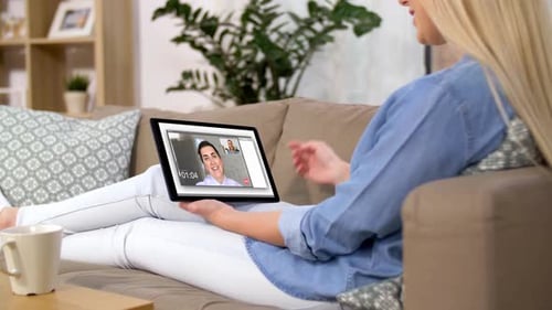 Woman waving hand on tablet computer during video call at home on sofa