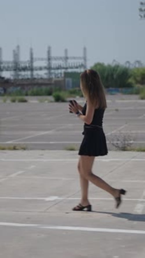 Young Girl Caucasian Woman in Short Black Dress Walking in Profile in Suburban Industrial Area Near