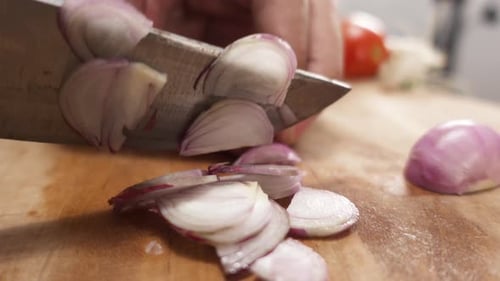 Close-up of a hand cutting an onion on a cutting board with a sharp knife, preparing ingredients for