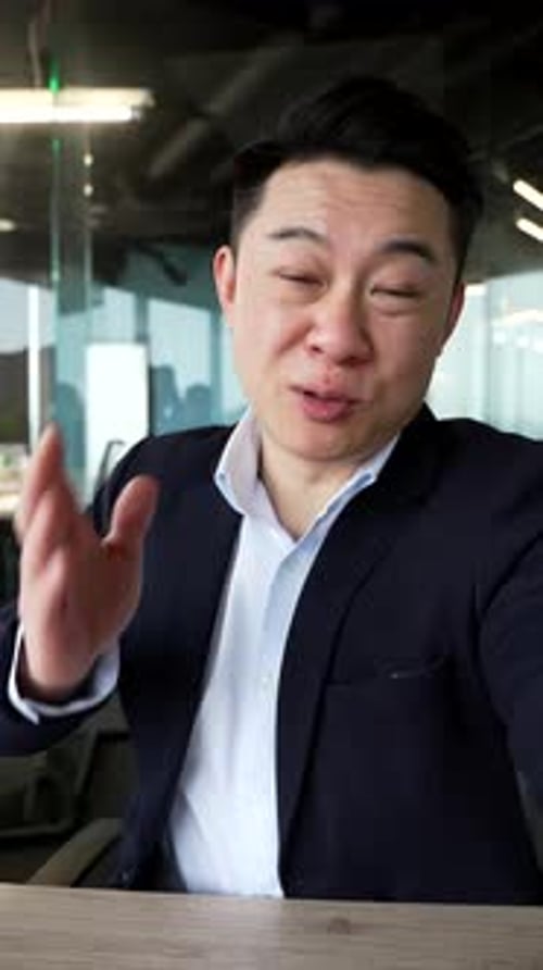 POV Vertical. Smiling asian businessman talking on a video call using a phone in office. Male worker