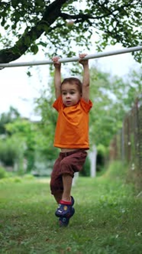 Little baby boy exercising on the horizontal bar outdoors. Caucasian kid doing sport. Vertical video