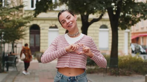 Smiling Woman Making Heart Shape on City Street