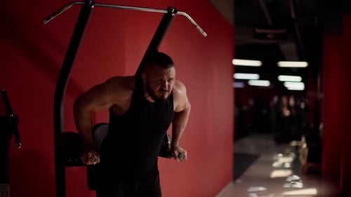 Muscular Man in Black Tank Top Performing Dip Exercise on Gym Machine Showcasing Upper Body Strength