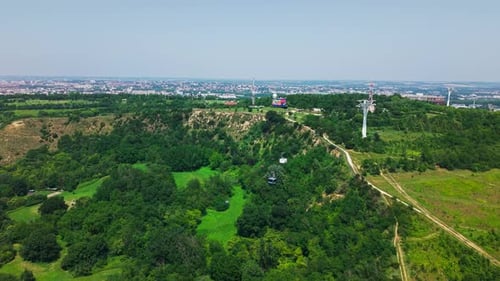 Aerial View of Green City Hillside with Cable Car Towers and Distant City
