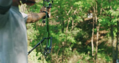 Slow motion close up of young man with professional equipment is practising archery with a bow in
