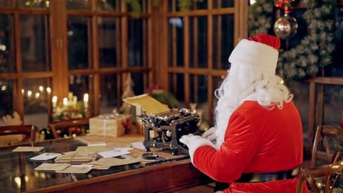Back view of Santa Claus sitting on the chair at and printing a letter on an old machine.