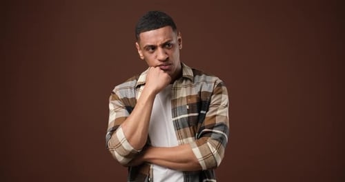 Young African American Man Thinking and Looking Up Standing Over Brown Studio Background