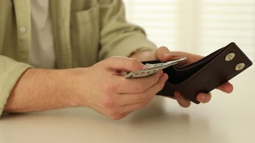 Man Counts Money from Wallet on White Table