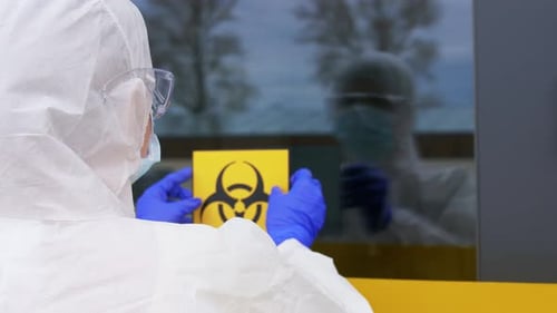 Worker in Protective Suit Attaching Biohazard Sign to Window