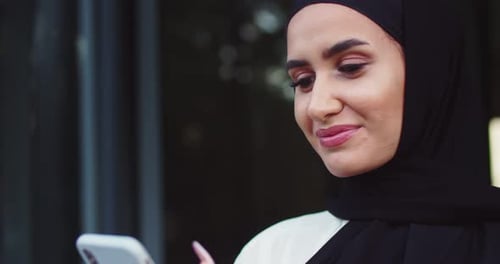 Close Up Portrait of Arabic Woman in Traditional Headscarves Looking at Phone and Smiling Pretty