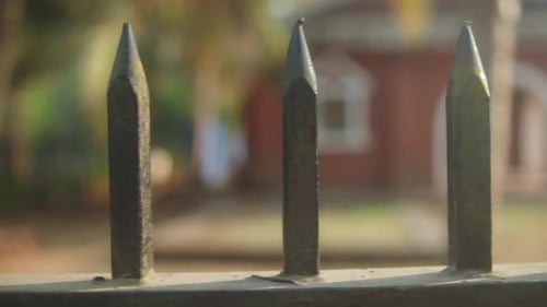 Close-up shot of sharp metal fence spikes, with a blurred garden or building in the background