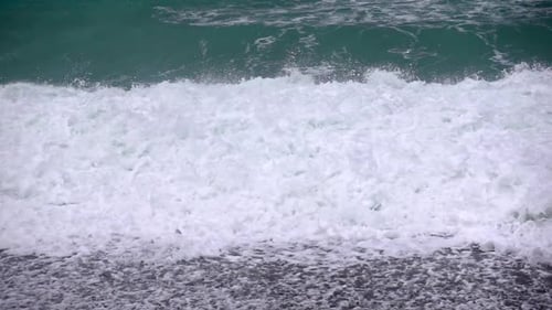 Storm waves powerfully crash against a pebble beach in slow motion