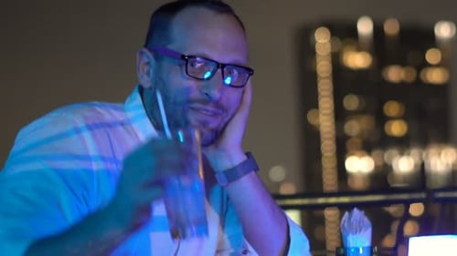 Handsome young man smiling raising a cocktail toast on a rooftop terrace bar at night