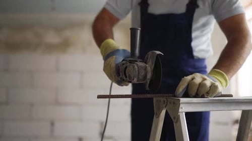 Professional Construction Worker's Hands in Work Gloves Using Angle Grinder to Cut Metal Rod at