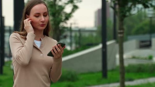 Portrait of a Young Woman Listening to Music on the Street with Wireless Headphones Using a