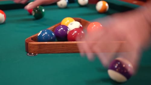 Person Racks 8 Ball Pool Triangle Closeup on the Spot gathering Solid and Stripped Billiard Balls on