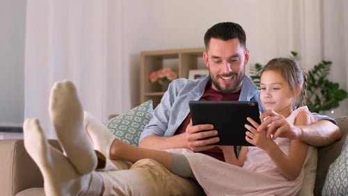 Father and daughter using tablet on couch indoors