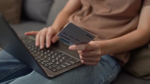 Woman holds credit card using laptop indoors