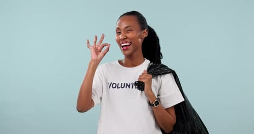 Cleaning trash bag, volunteer and black woman okay sign for garbage pollution project