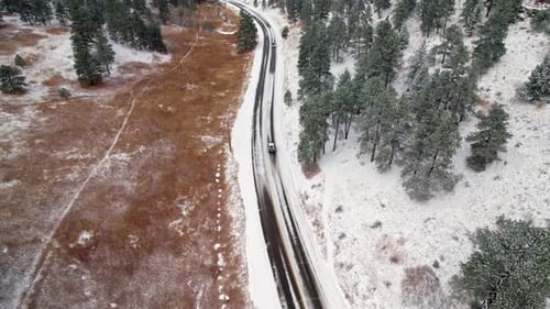 Drohnen-Luftaufnahme von Autos, die auf der verschneiten Winterlandstraße im Pine Tree Woodland Hills Valle fahren