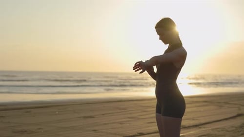 Woman Checks Smartwatch on Beach at Sunrise