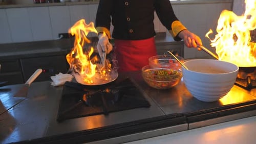 Unrecognizable Chef Holding Two Flaming Pans and Cooking Tasty Flambe Style Dish in Modern Kitchen